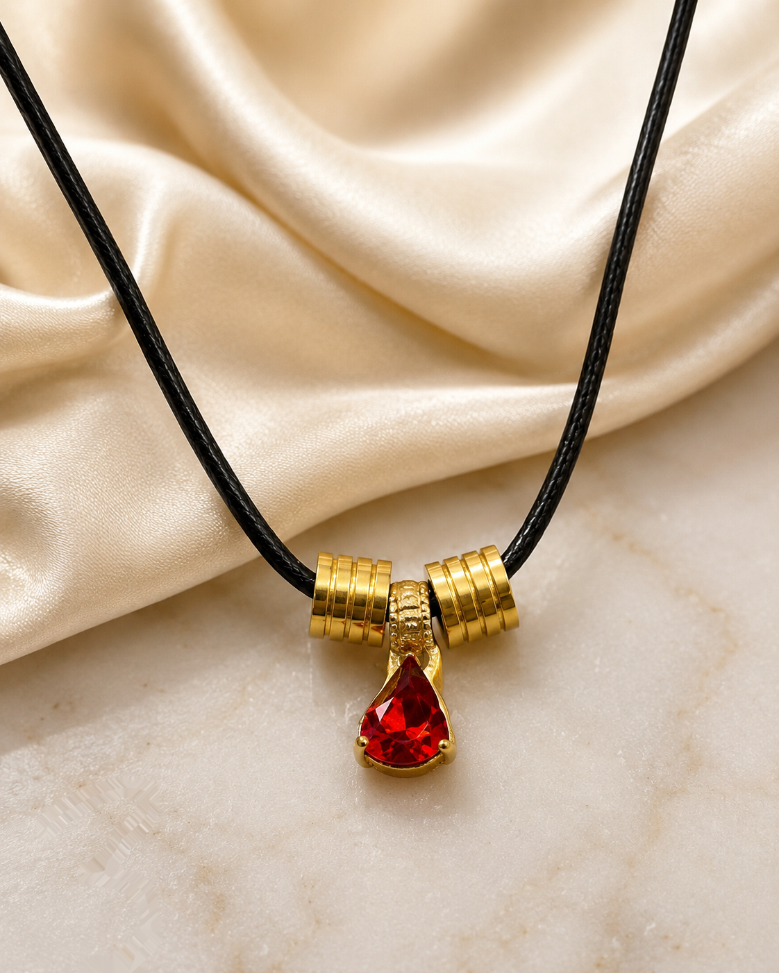 Black cord necklace with a gold-toned pendant and red teardrop stone